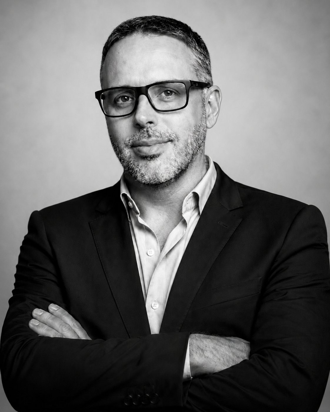 Retrato institucional de Alex Lima de braços cruzados, terno escuro sobre fundo neutro, preto e branco